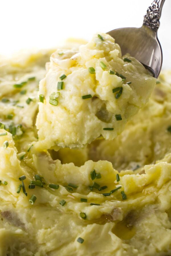 Close-up of mashed potatoes with chives, melted butter, and spoon serving.