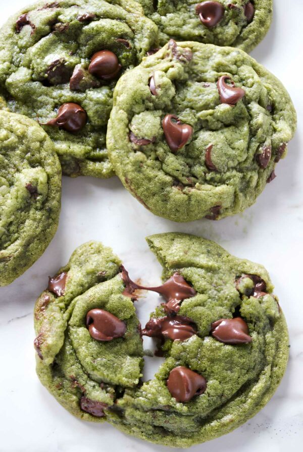 Green matcha chocolate chip cookies with melted chips on marble surface.