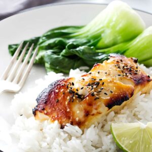 Miso glazed sea bass, white rice, bok choy, and lime on a plate.