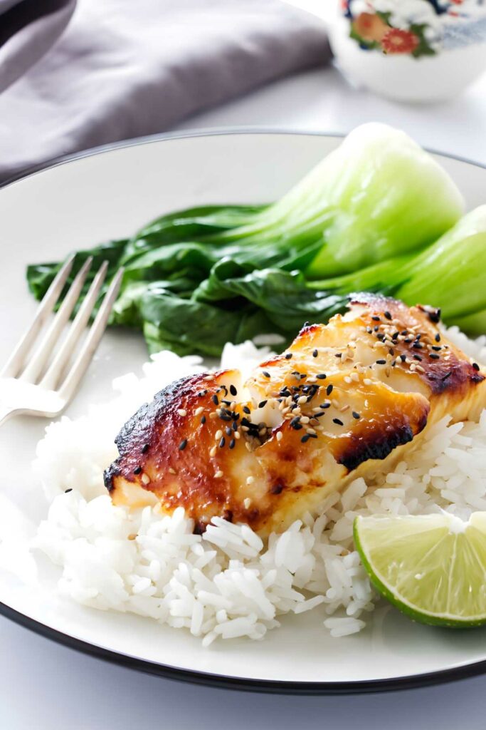 Miso glazed sea bass, white rice, bok choy, and lime on a plate.