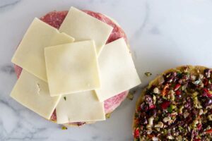 adding more cheese to the muffuletta recipe.