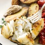 Close-up of sea bass white fish with herbs, potatoes, tomatoes, and fork.
