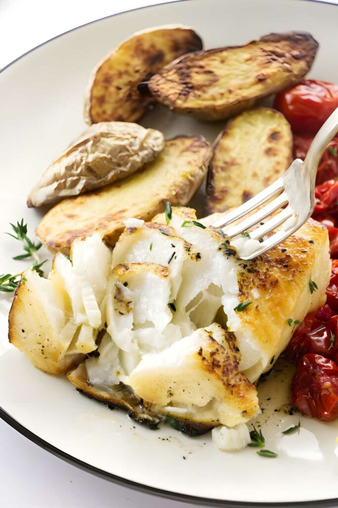 Close-up of sea bass white fish with herbs, potatoes, tomatoes, and fork.