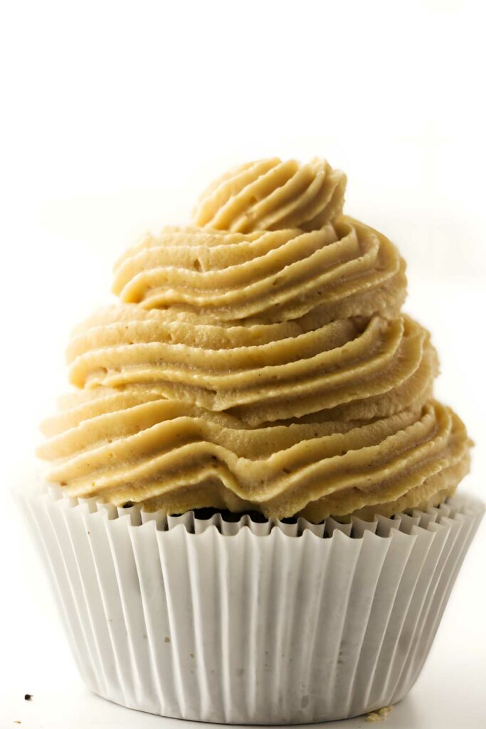 Close-up of cupcake with light brown frosting in white paper liner.