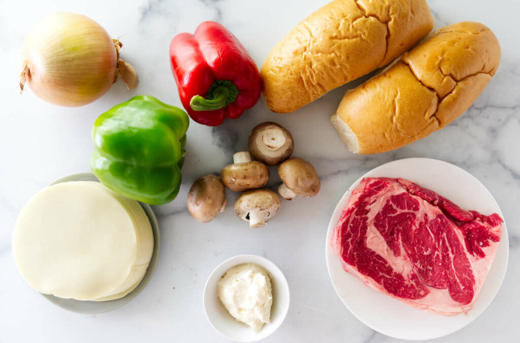 Philly cheesesteak ingredients on a marble counter.