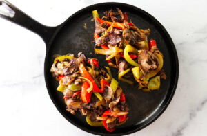 Adding toppings to philadelphia cheesesteak recipe in a skillet.