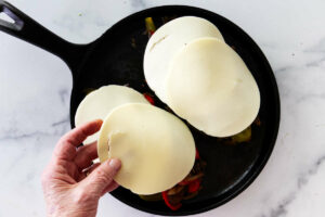 Adding cheese to the top of philadelphia cheese steak sandwich.