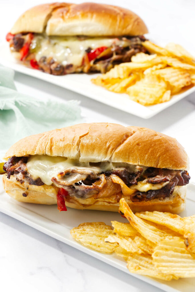 A philly cheese sandwich recipe and potato chips on a plate.