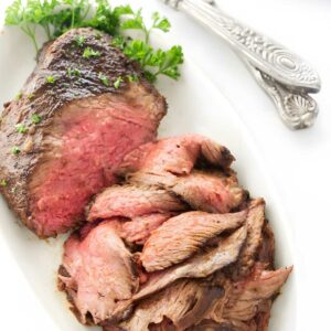 Sliced tri tip on plate with parsley, serving utensils.