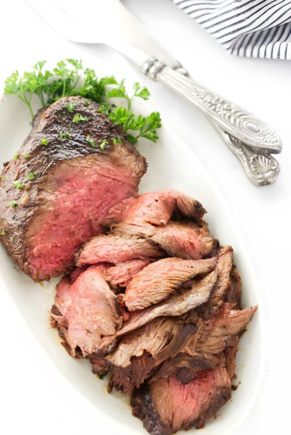 Sliced tri tip on plate with parsley, serving utensils.