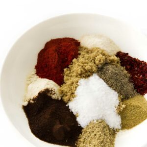 White bowl with assorted colorful spice powders arranged in small mounds.