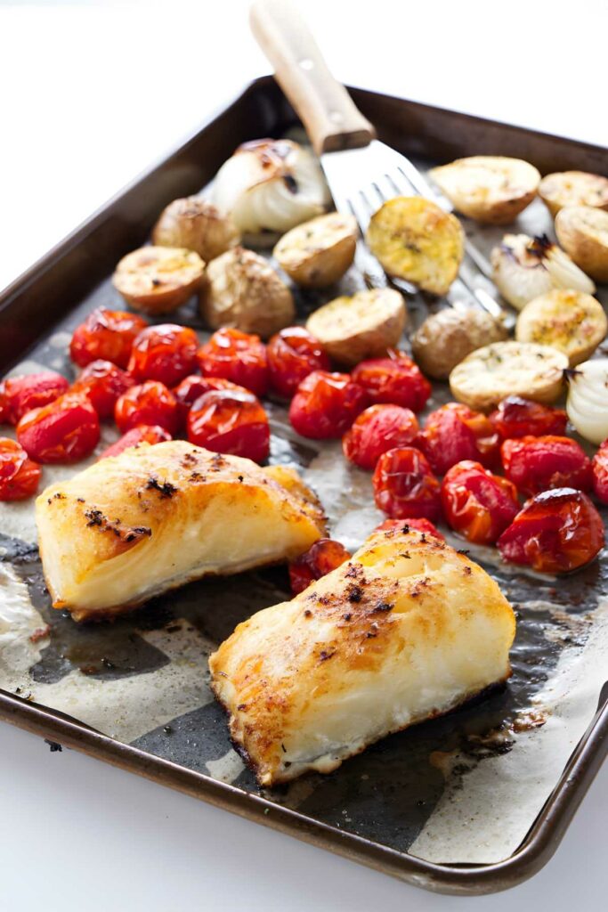 Roasted sea bass, potatoes, tomatoes, and onions on a baking sheet.