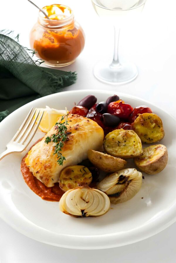Baked sea bass dinner with vegetables, red sauce, and glass of wine.