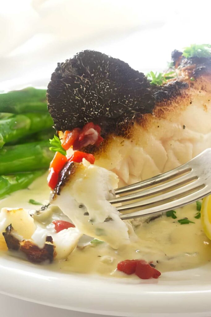 A sea bass fillet on a plate with truffle butter sauce.