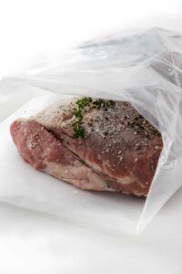 Seasoned tri tip with herbs in vacuum bag, prepared for sous vide.