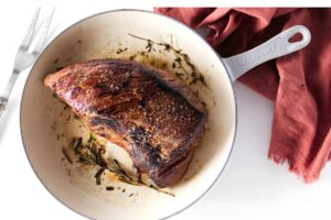 Browned tri tip with herbs in white skillet.