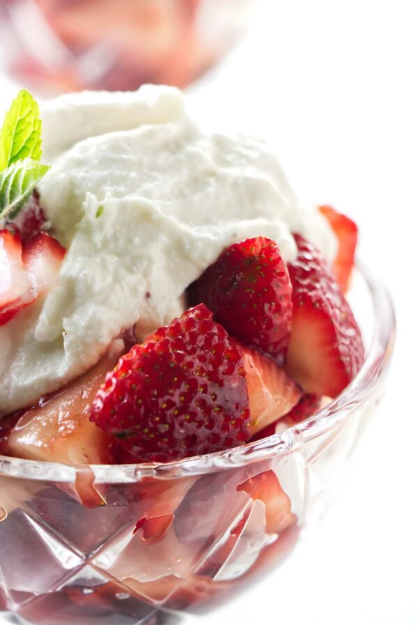 Strawberries with whipped ricotta and mint leaf in a glass bowl.