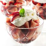 Strawberries and whipped cream in glass bowls, topped with mint leaves.