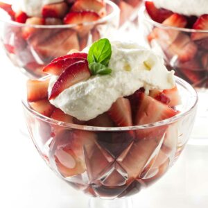 Strawberries and whipped cream in glass bowls, topped with mint leaves.