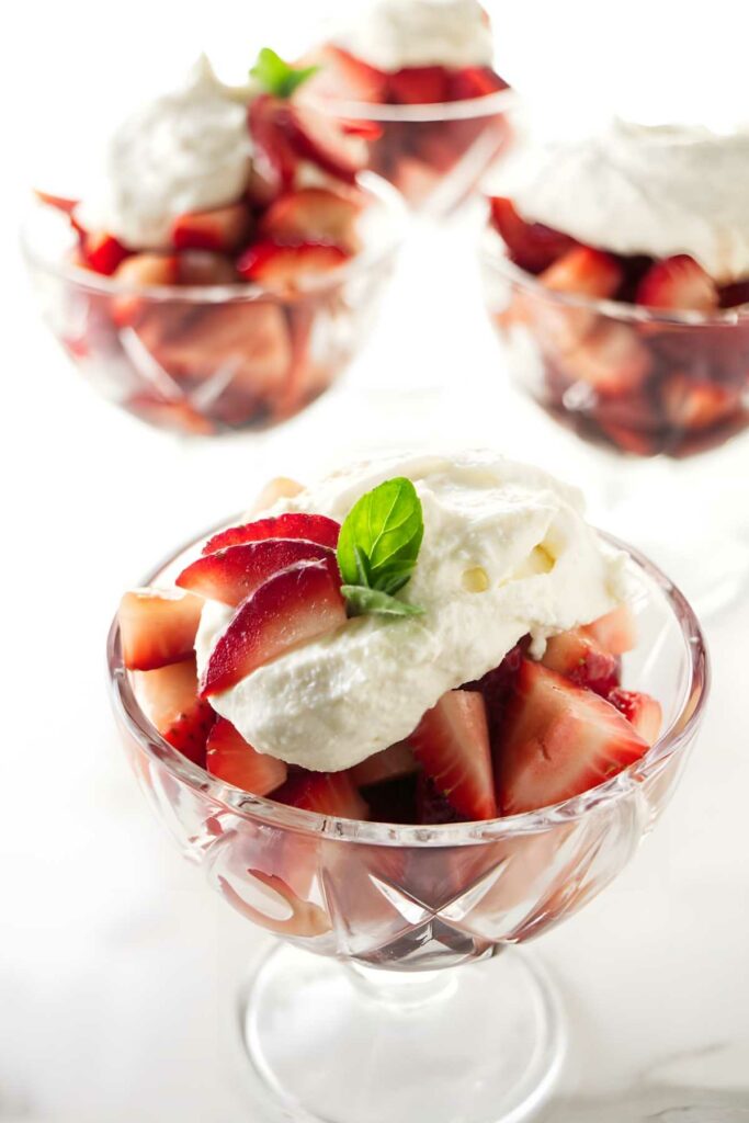 Bowls of chopped strawberries with ricotta and mint on white surface.