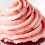 Close-up of a cupcake with pink swirled frosting in white liner.
