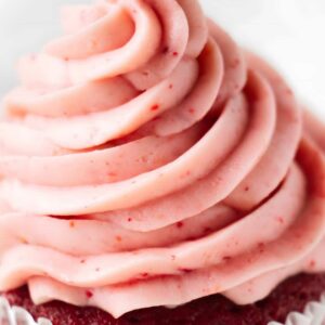 Close-up of a cupcake with pink swirled frosting in white liner.