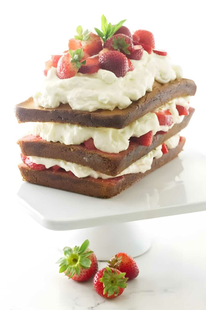 Three-layer strawberry shortcake with whipped cream, on white stand, fresh strawberries.