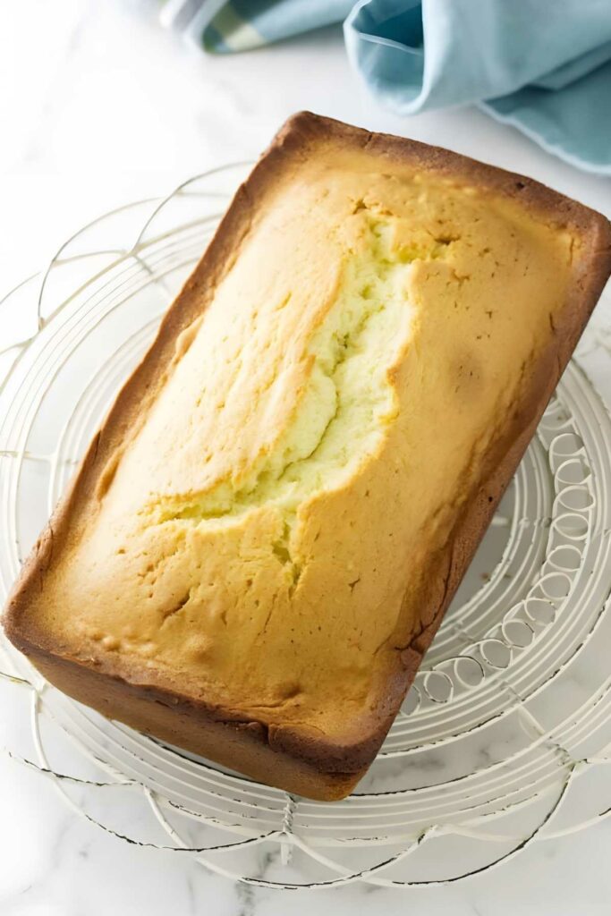 Golden-brown pound cake loaf on wire rack, marble background, blue cloth.