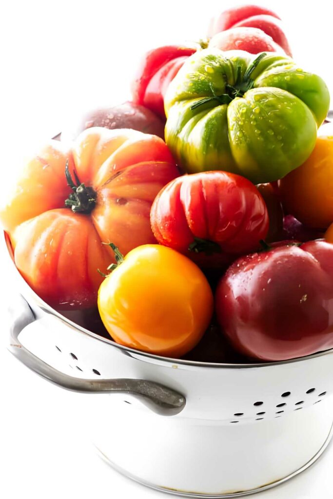 Colander of colorful heirloom tomatoes with water droplets.