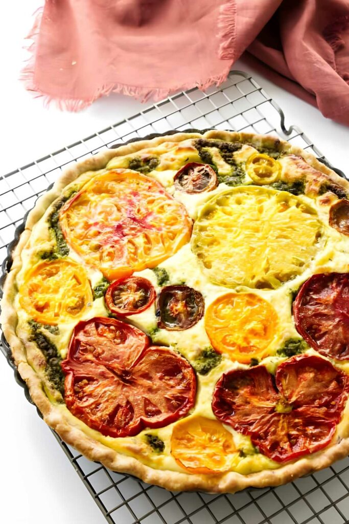 Colorful ricotta cheese tomato tart with pesto on wire rack.