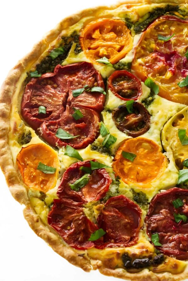 Colorful vegetable tart topped with sliced tomatoes, basil, and pesto swirl.