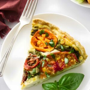 Slice of tomato-topped vegetable quiche with salad and basil on plate.
