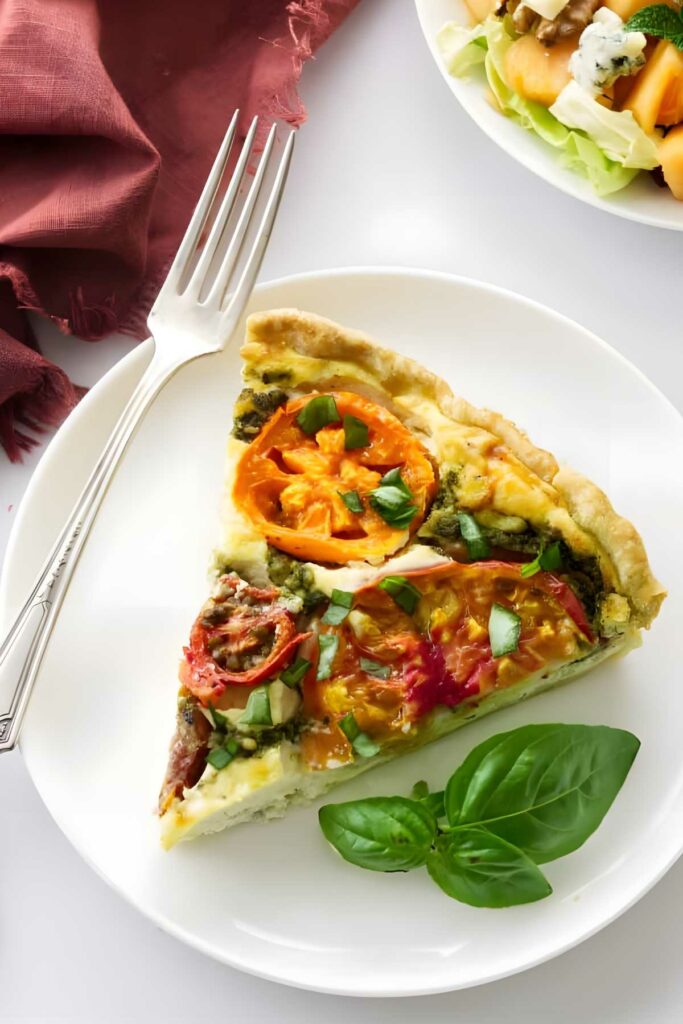 Slice of ricotta tomato quiche with salad and basil on plate.