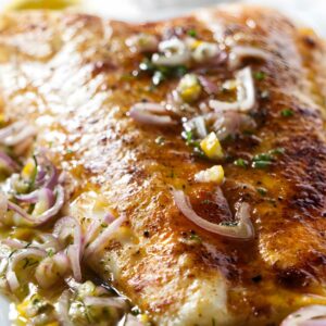 Cooked fish fillet with onion-herb sauce, lemon wedge, and extra sauce.