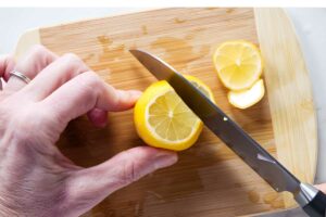 Hand slicing lemon on wooden cutting board.