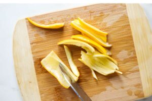 Knife slicing lemon peel on a cutting board.