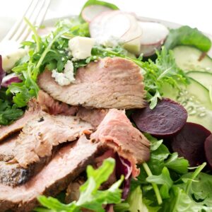 Tri tip Steak salad with mixed greens, vegetables, crumbled cheese, and a fork.