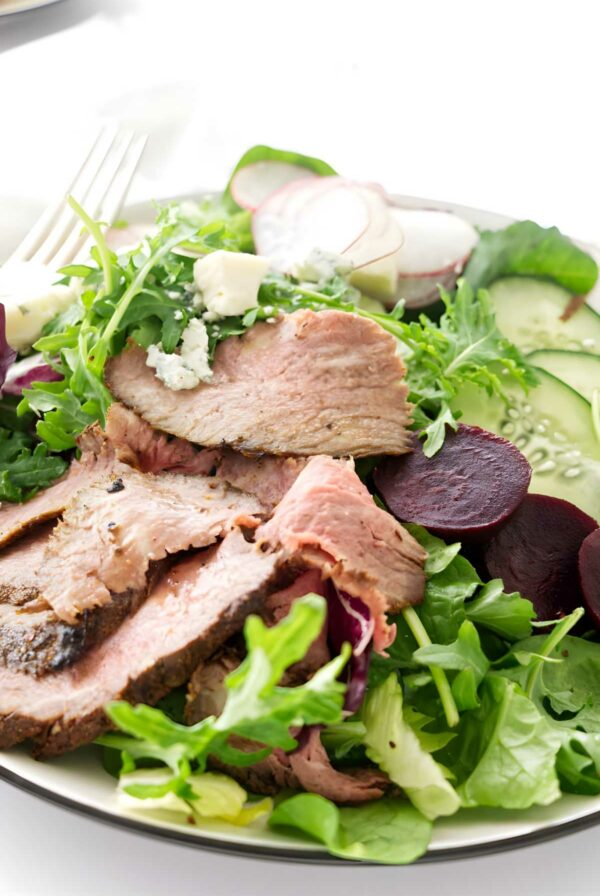 Tri tip Steak salad with mixed greens, vegetables, crumbled cheese, and a fork.