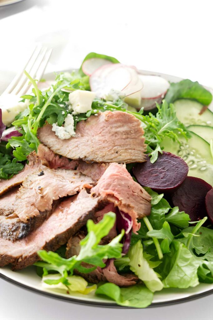 Steak salad made with leftover tri tip and with mixed greens, vegetables, crumbled cheese, and a fork.