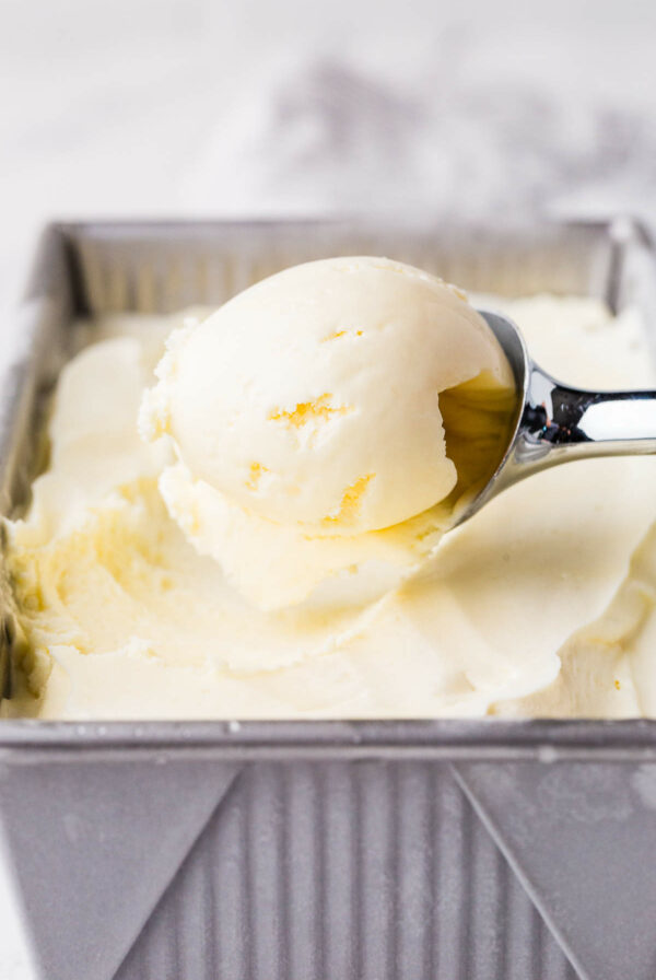 Scooping homemade vanilla ice cream from a metal container.