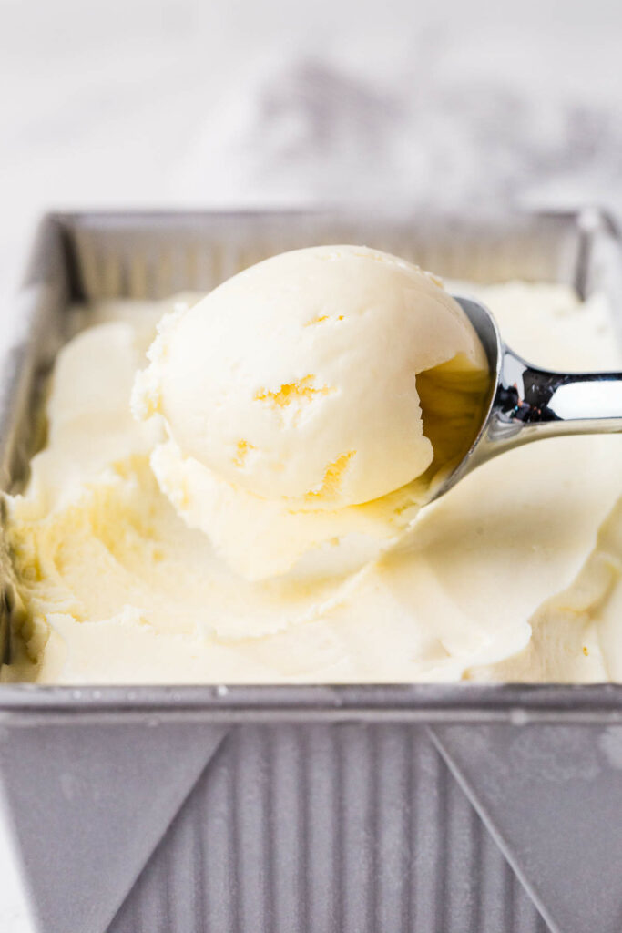 Scooping homemade vanilla ice cream from a metal container.
