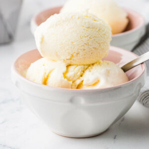Vanilla ice cream scoops in a white bowl with spoon.