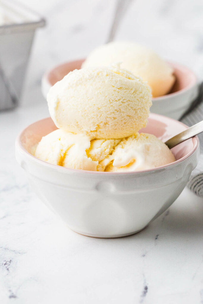 Vanilla ice cream scoops in a white bowl with spoon.