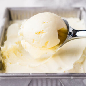 Metal scoop lifting vanilla ice cream from tray.