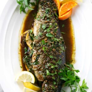 Whole cooked fish with herbs, citrus wedges, parsley, and brown sauce.