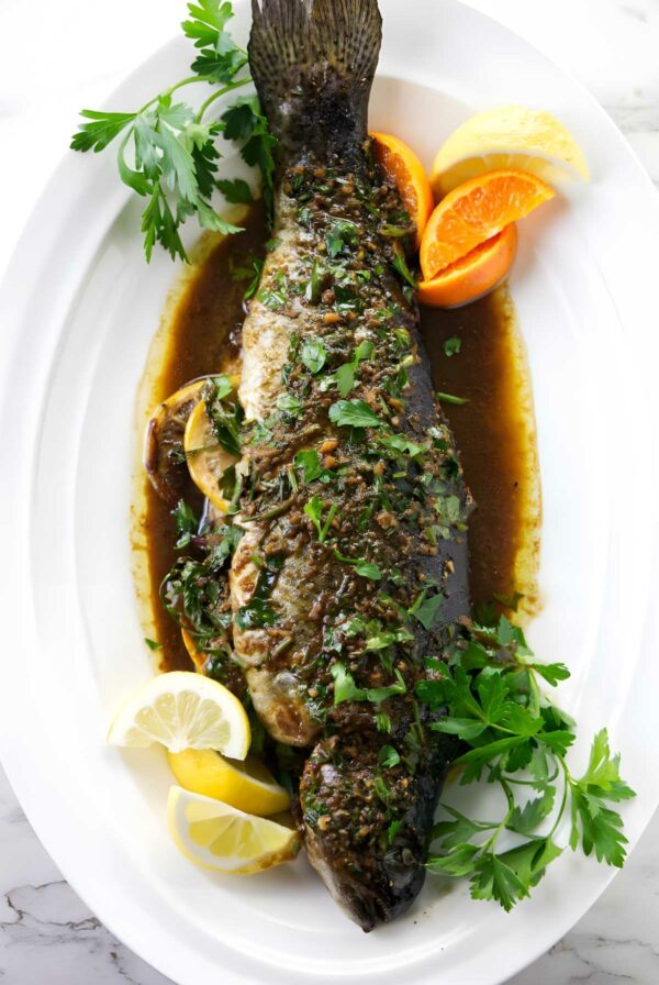 Whole baked rainbow trout with herbs, citrus wedges and sauce.