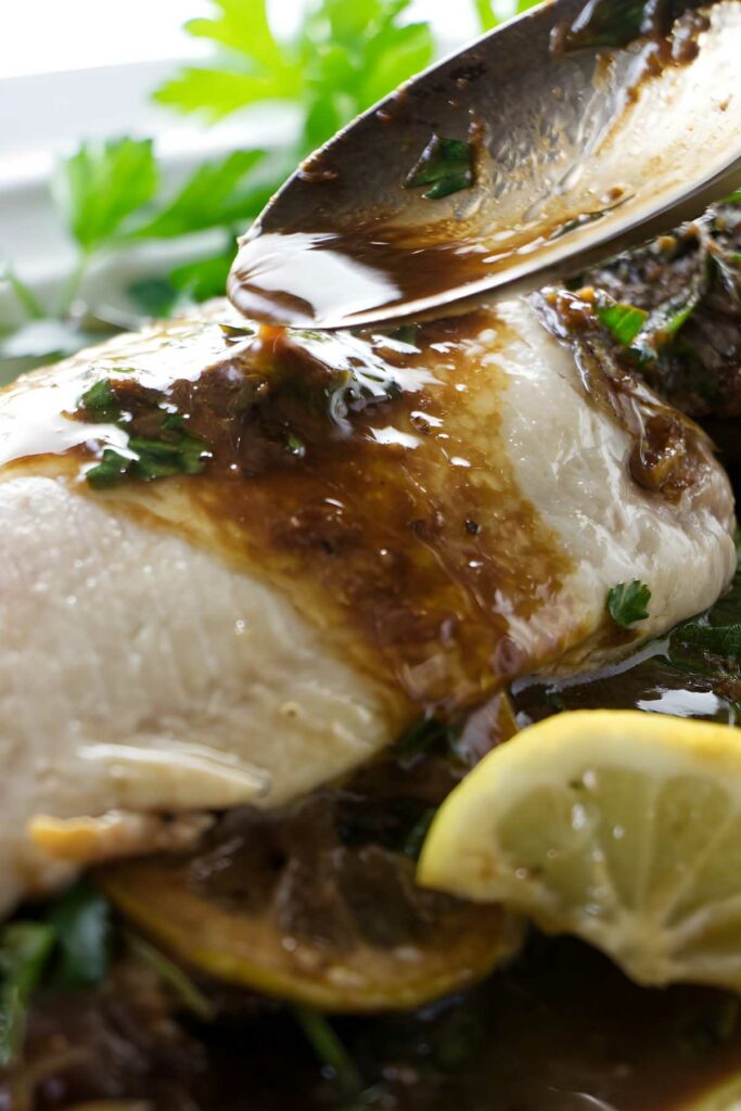 Spoon pouring sauce over cooked rainbow trout. 