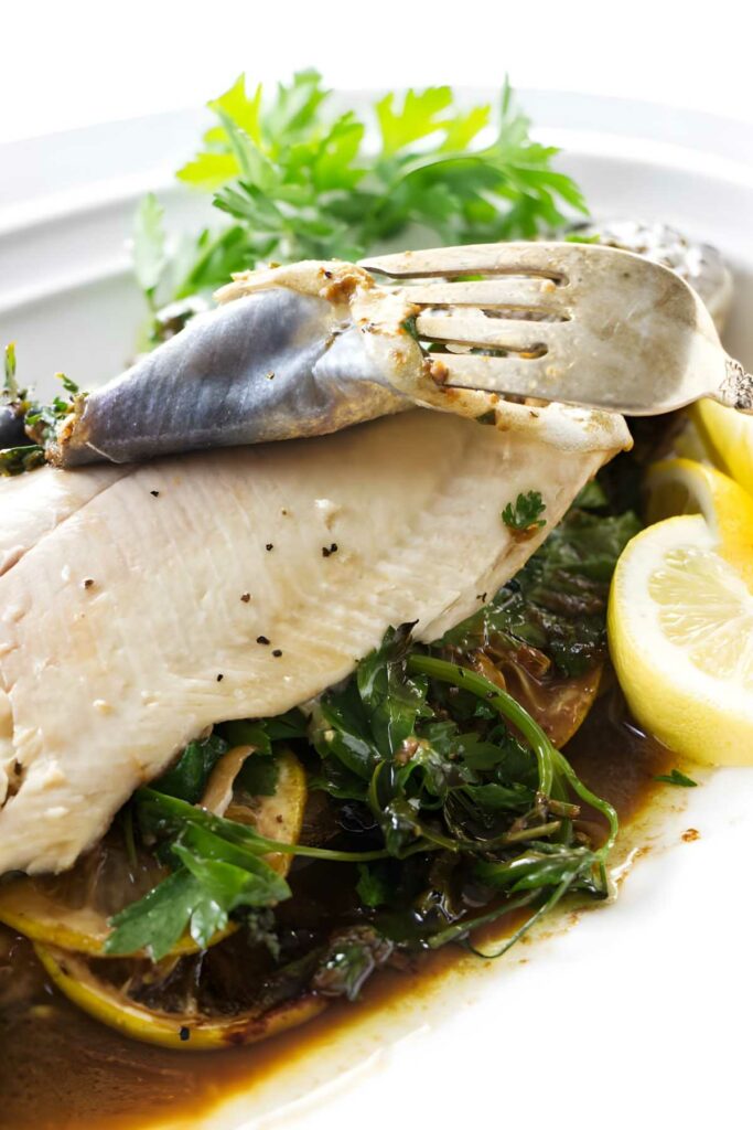 Fork holds flaky trout with herbs and sauce.