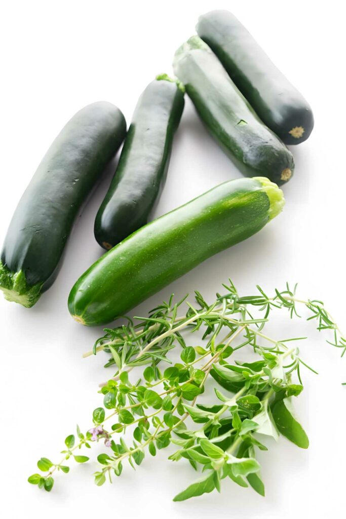 Five fresh zucchinis with thyme and rosemary on a white background.