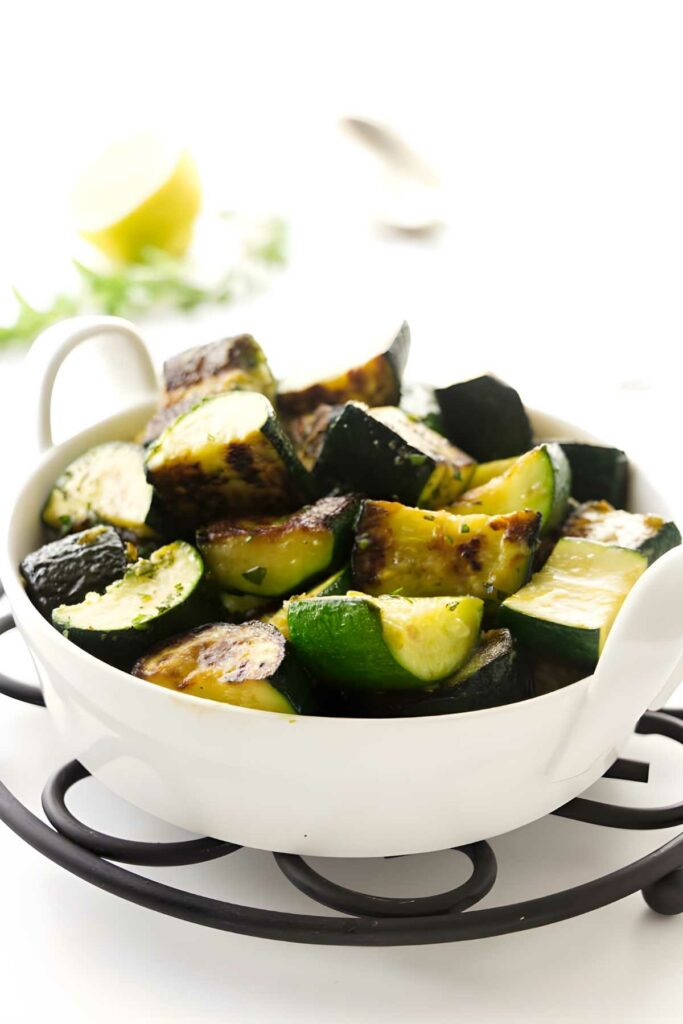 Charred sauteed zucchini slices in white bowl on black trivet.